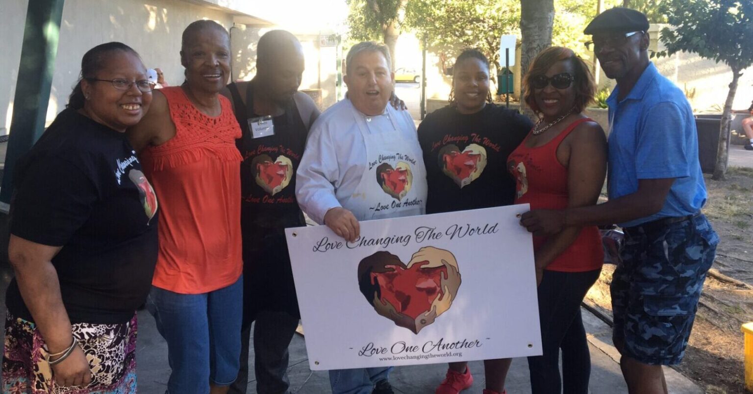 A group of people standing together holding a Love Changing The World Sign