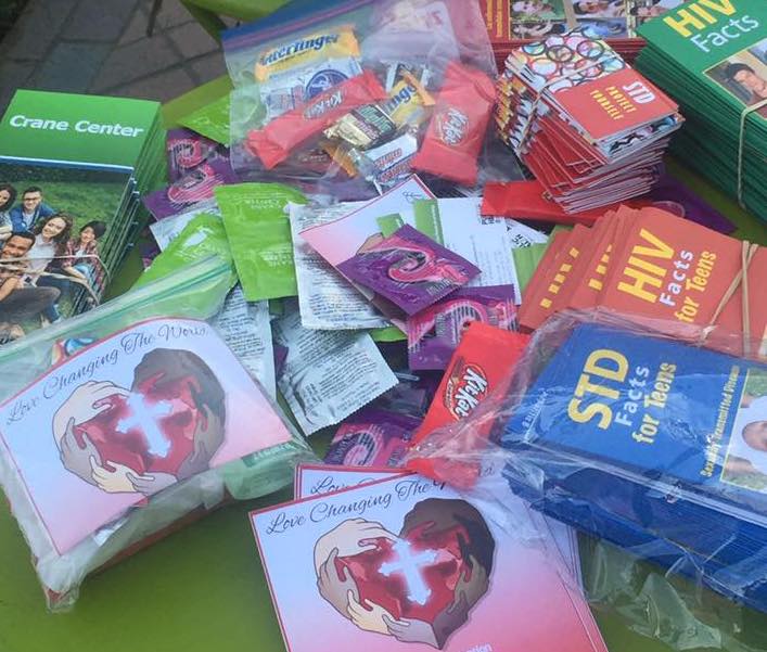 Close-up view of Love Changing The World, Inc. outreach supplies including condom packets, candy bags, HIV and STD educational pamphlets, and prevention materials prepared for community health distribution.