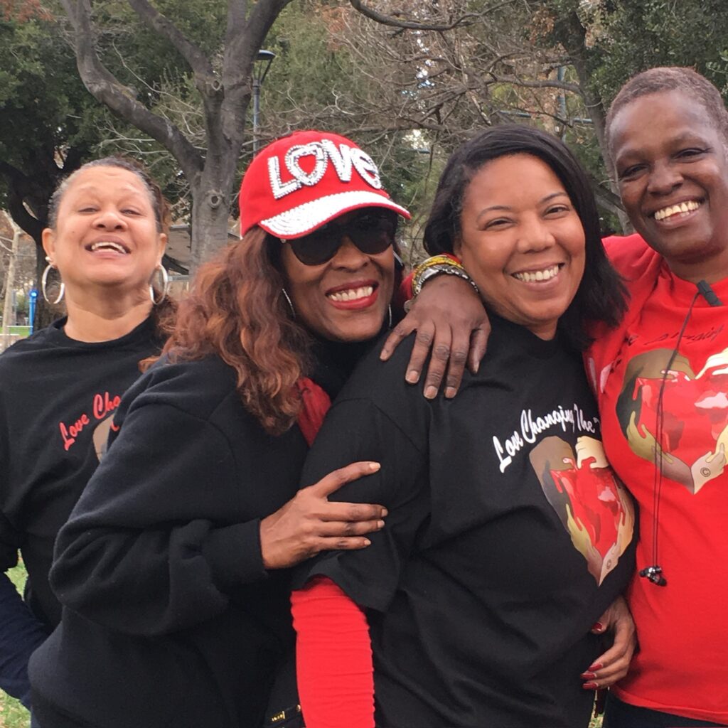 Four lady volunteers, smiling and standing wearing red and black Love Changing the World shirts.